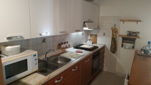 A kitchen with white cabinets, a stainless steel sink, a microwave, and a stove. - Mediterranean Idyll (Sardegna)