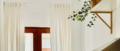 Una cocina moderna con encimera de madera, armarios blancos, horno empotrado y ventana con cortinas blancas.