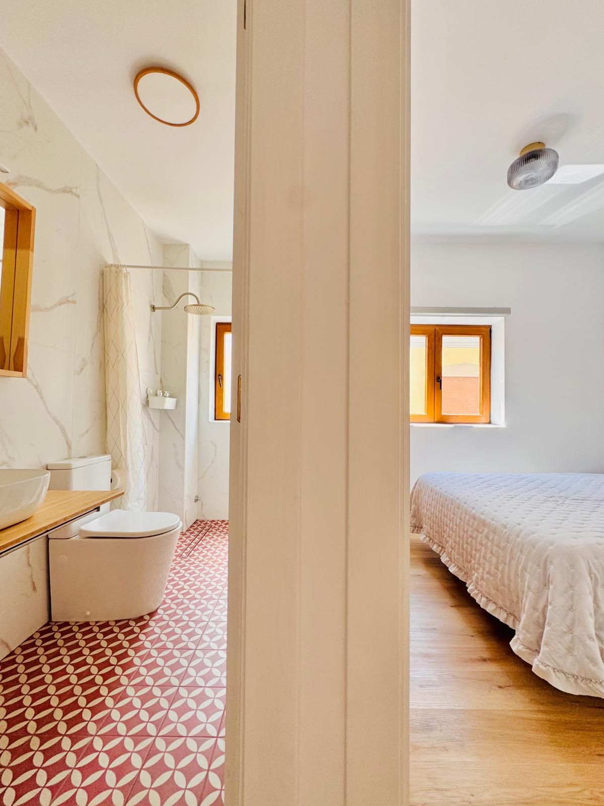 Un baño moderno con pared de mármol, tocador de madera, inodoro blanco y piso estampado.