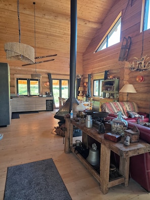 L’intérieur d’un chalet rustique, avec une grande cheminée, des meubles en bois et une vue sur l’extérieur.