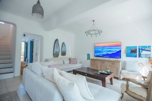 Una sala de estar moderna con un sofá, una mesa de centro y un televisor de pantalla plana. Hay dos cuadros en la pared, una araña y una escalera que lleva a otra habitación.
