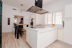 Een moderne keuken met witte kasten, een centraal eiland, een inbouwoven en een plafondventilator.