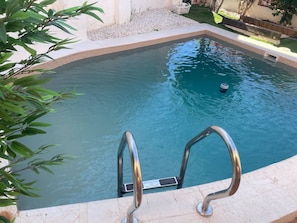 Una piscina con una escalera metálica y un borde de piedritas.