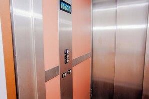 Een liftinterieur met metalen wanden, een veiligheidssignaal en knoppen voor de verdiepingen.