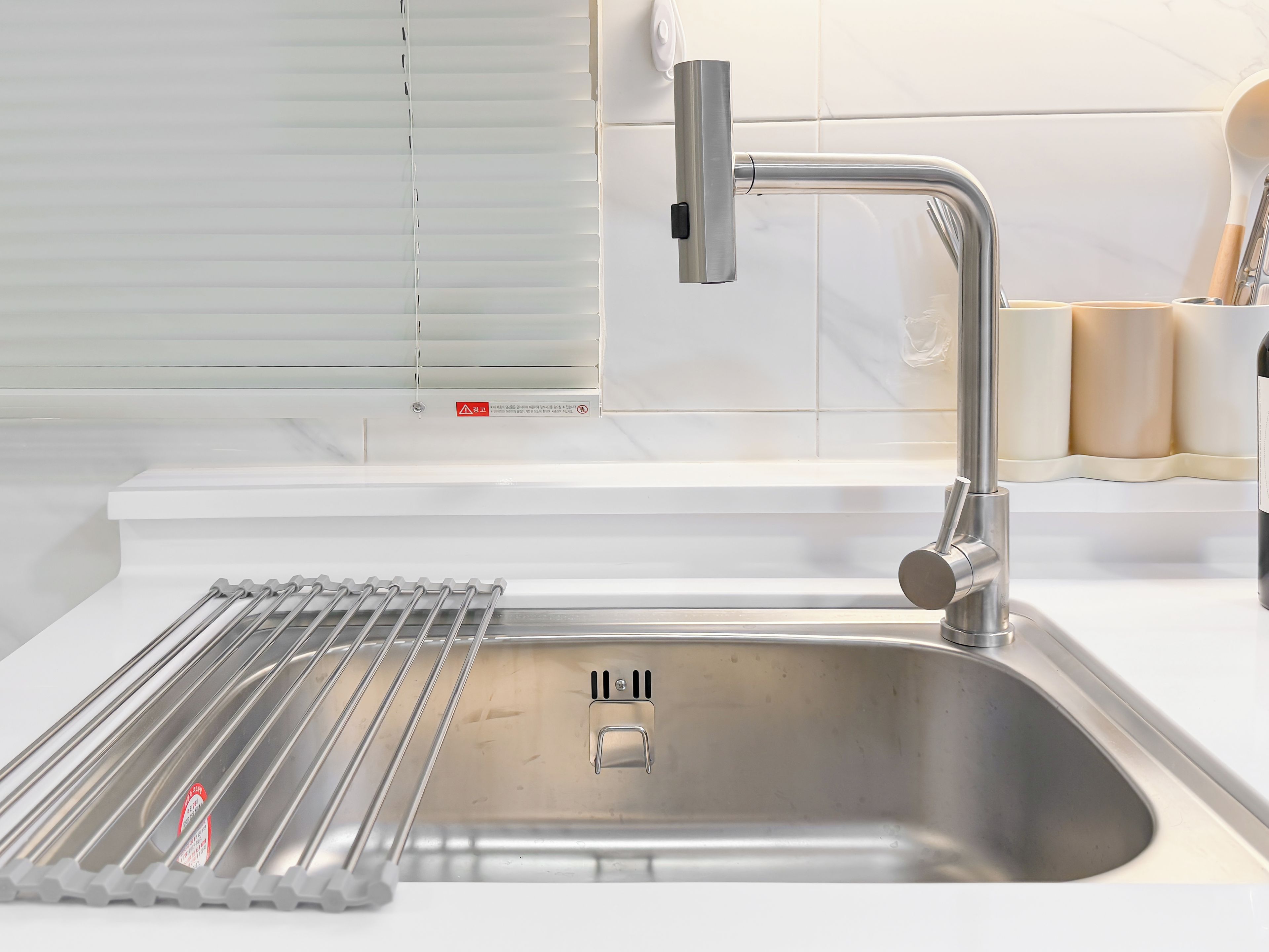 A modern kitchen with a stainless steel sink, a faucet, and a window with blinds.