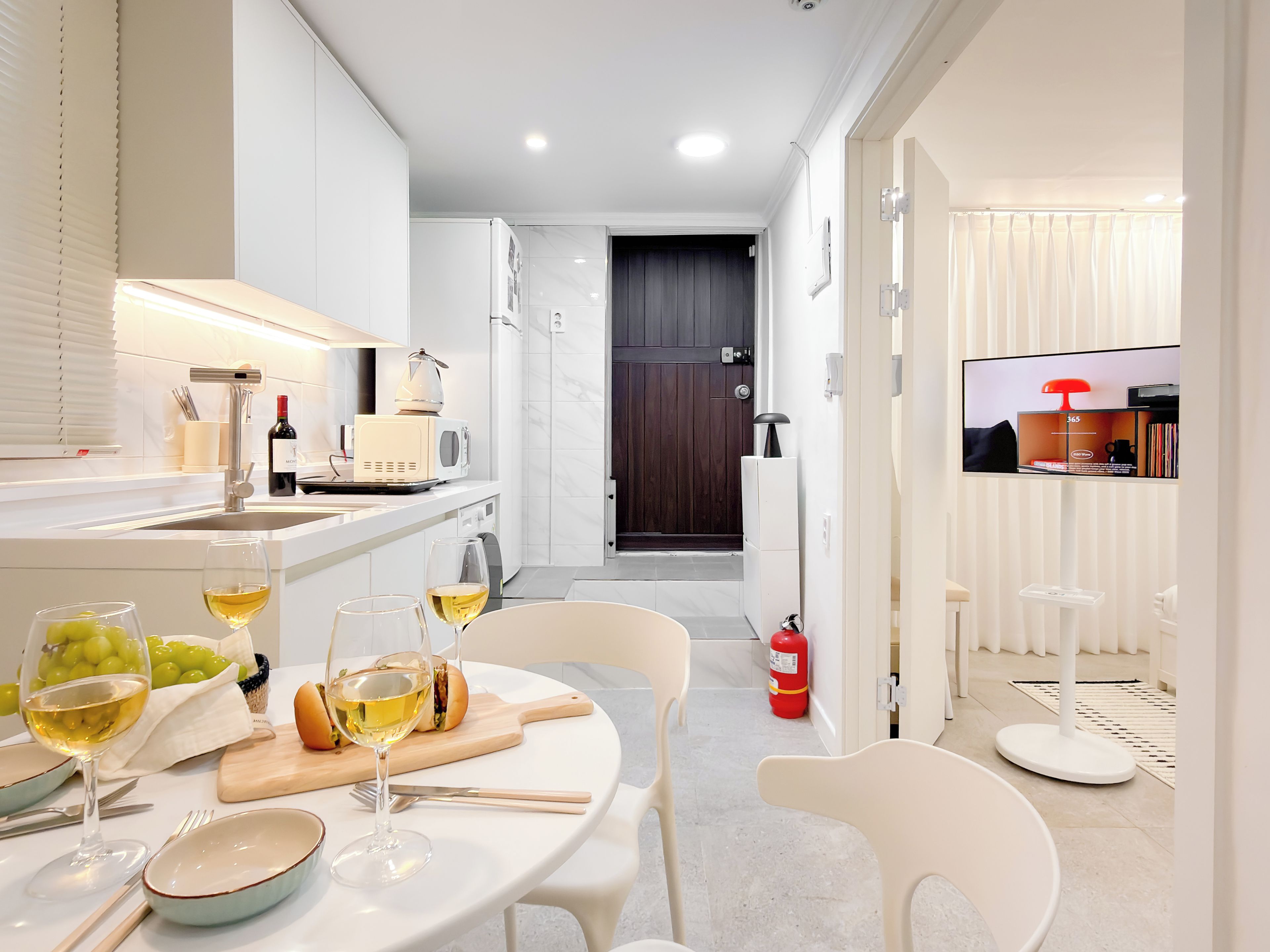 A modern kitchen with white appliances, a dining area with a table set for two, and a TV mounted on the wall.