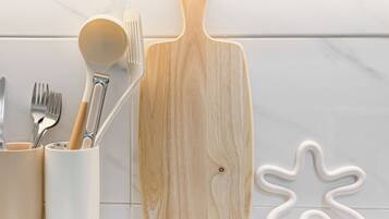 A kitchen counter with a wooden cutting board, a white ceramic spoon, and a white ceramic fork holder.