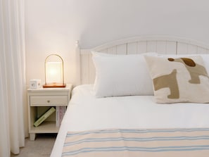 Una cama bien hecha con un edredón a rayas, una mesita de noche blanca con una lámpara y un libro titulado 'Book of Jam'.