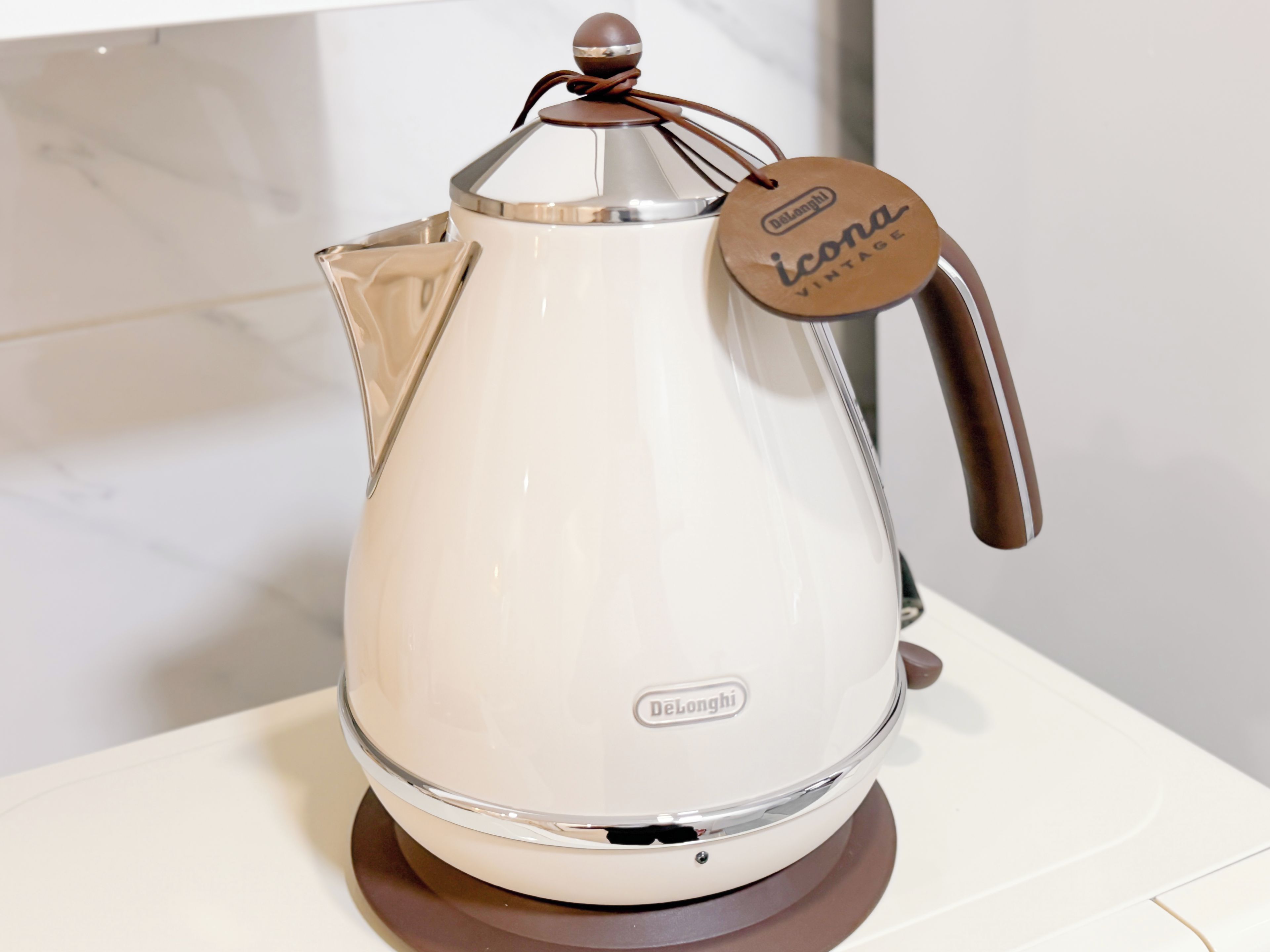 A white DeLonghi electric kettle with a brown handle and a vintage tag.