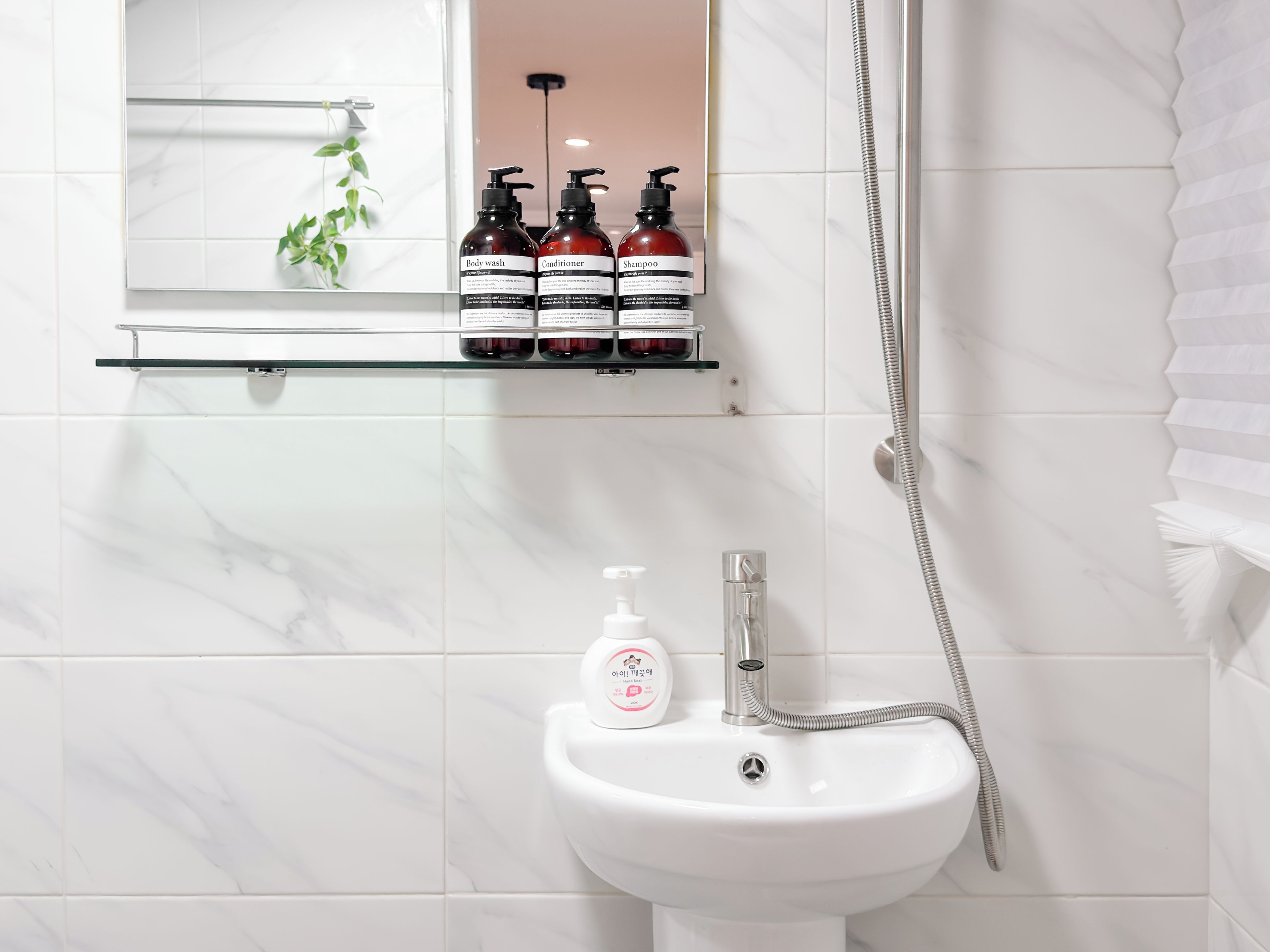A bathroom with a white sink, a mirror, and a shelf with three bottles of toiletries.