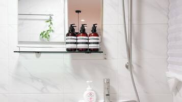 A bathroom with a white sink, a mirror, and a shelf with three bottles of toiletries.