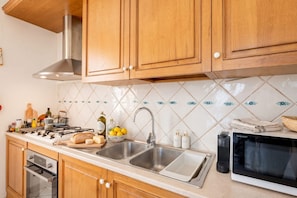 Una cocina con armarios de madera, un lavamanos de acero inoxidable, un microondas y diversos utensilios de cocina sobre la encimera.