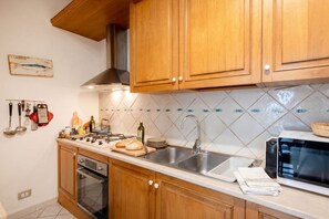 A kitchen with wooden cabinets, a gas stove, a sink, and a microwave. - Historic Stone Loft in the Heart of Bari (Bari)