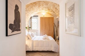 A bedroom with a bed, a wooden wardrobe, a window, and a stone archway. - Historic Stone Loft in the Heart of Bari (Bari)