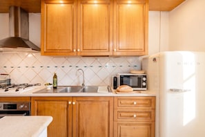 Una cocina con armarios de madera, microondas, refrigerador, lavamanos y estufa.