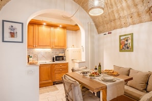 A cozy kitchen with wooden cabinets, a dining table set for two, and a sofa in the adjacent living area. - Historic Stone Loft in the Heart of Bari (Bari)