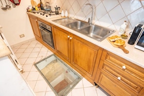 A kitchen with wooden cabinets, a stainless steel sink, a gas stove, and a glass door leading to a storage area. - Historic Stone Loft in the Heart of Bari (Bari)