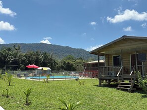 A wooden cabin with a porch, a fenced pool area, and a mountain backdrop.
