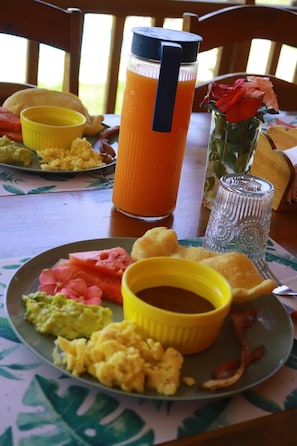 A breakfast setting with a plate of scrambled eggs, avocado, and bacon, a glass of orange juice, and a yellow mug.