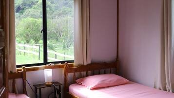 A bedroom with a wooden four-poster bed, a bedside table with a lamp, and a window with curtains.