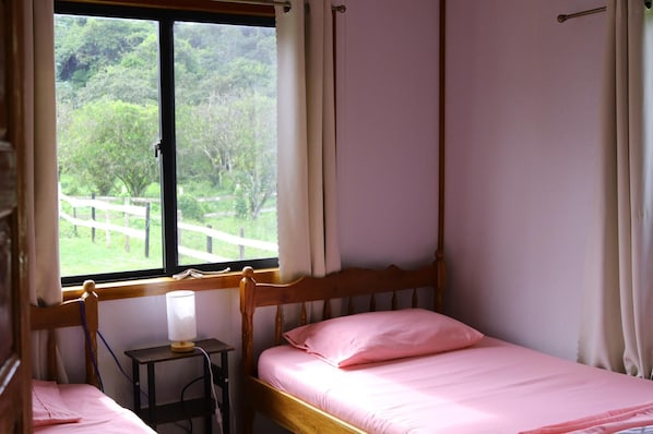 A bedroom with a wooden four-poster bed, a bedside table with a lamp, and a window with curtains.