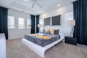 Ein modernes Schlafzimmer mit einem gebogenen Bett, einem Deckenventilator und großen Fenstern mit Jalousien.