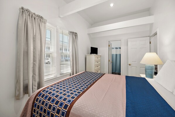 A bedroom with a bed, a dresser, a television, a lamp, and a door.