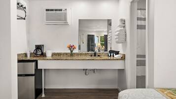 A compact kitchenette with a built-in refrigerator, a coffee maker, and a sink with a granite countertop.