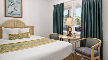 A hotel room with a bed, two chairs, a table with a lamp, a painting on the wall, and a window with curtains.