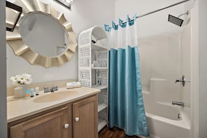 A bathroom with a round mirror, a sink, a toilet, and a shower area. - sea shell motel (Chincoteague)