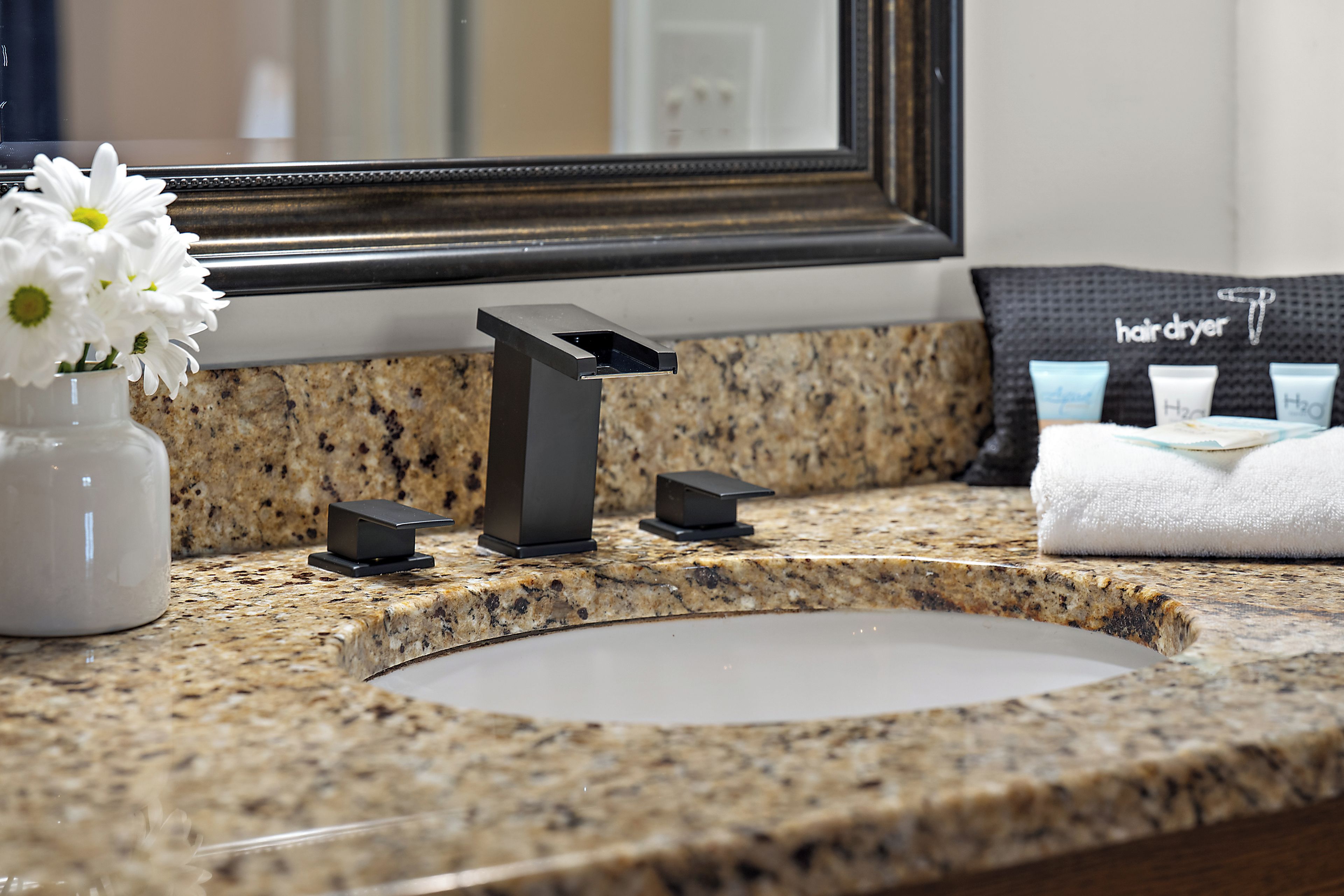 A bathroom with a granite countertop, a sink, a mirror, a towel, and a hairdryer.