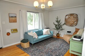 Ein Wohnzimmer mit einem blauen Sofa, einem gemusterten Teppich, einem grünen Schrank und einer Pflanze.
