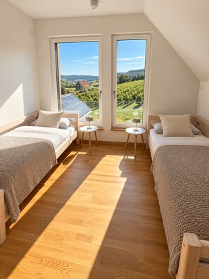 Un dormitorio con dos camas, una mesita y vistas a un viñedo a través de amplias ventanas.