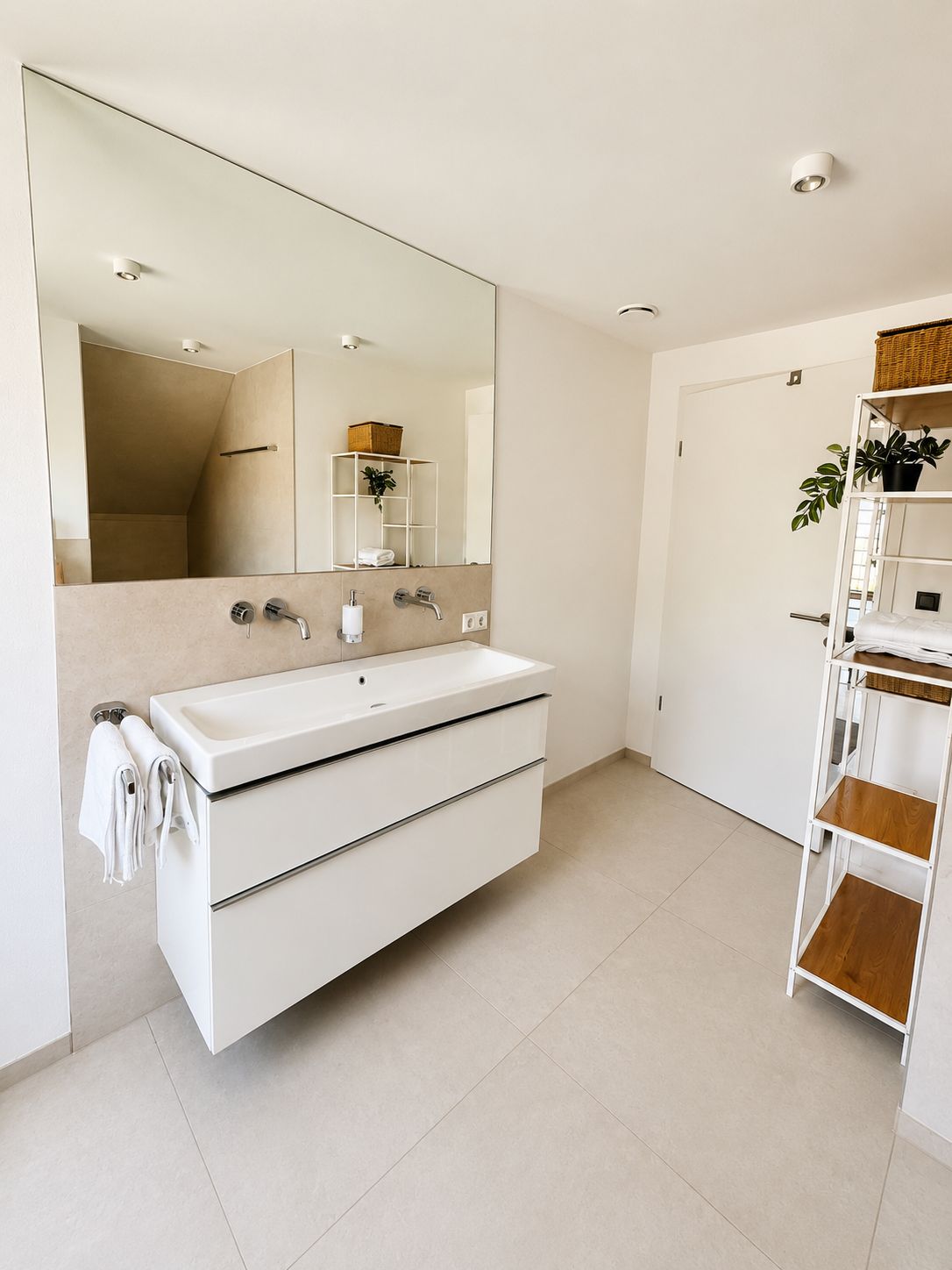 Une salle de bain moderne avec un grand miroir, un meuble-lavabo blanc et une étagère en bois.