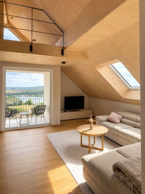 Ein geräumiges Loft mit einem großen Oberlicht, einem Balkon mit Sitzgelegenheiten, einer Couch und einem Fernseher.