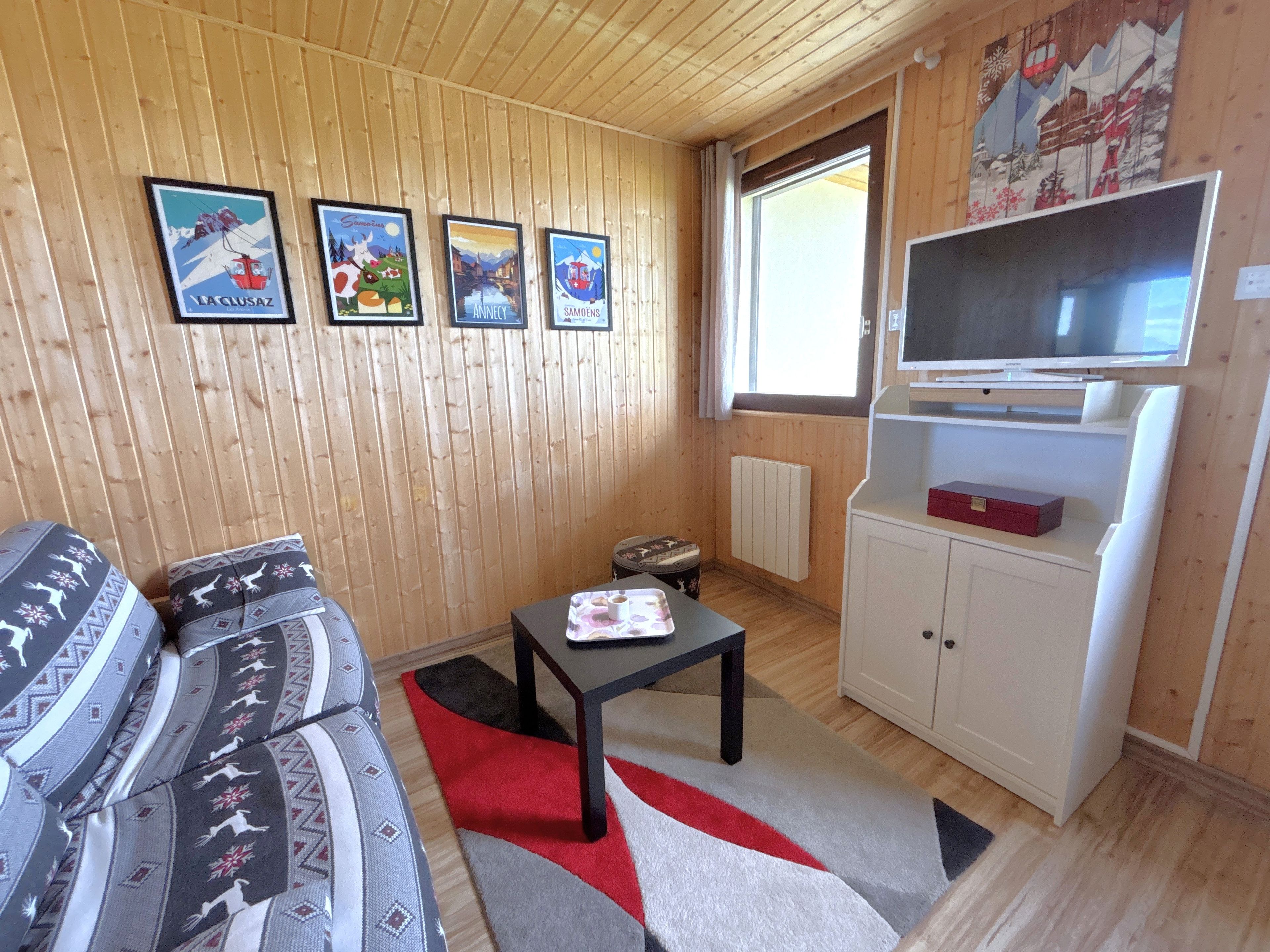 A wooden-paneled room with a sofa, a small table, a television, and a radiator.