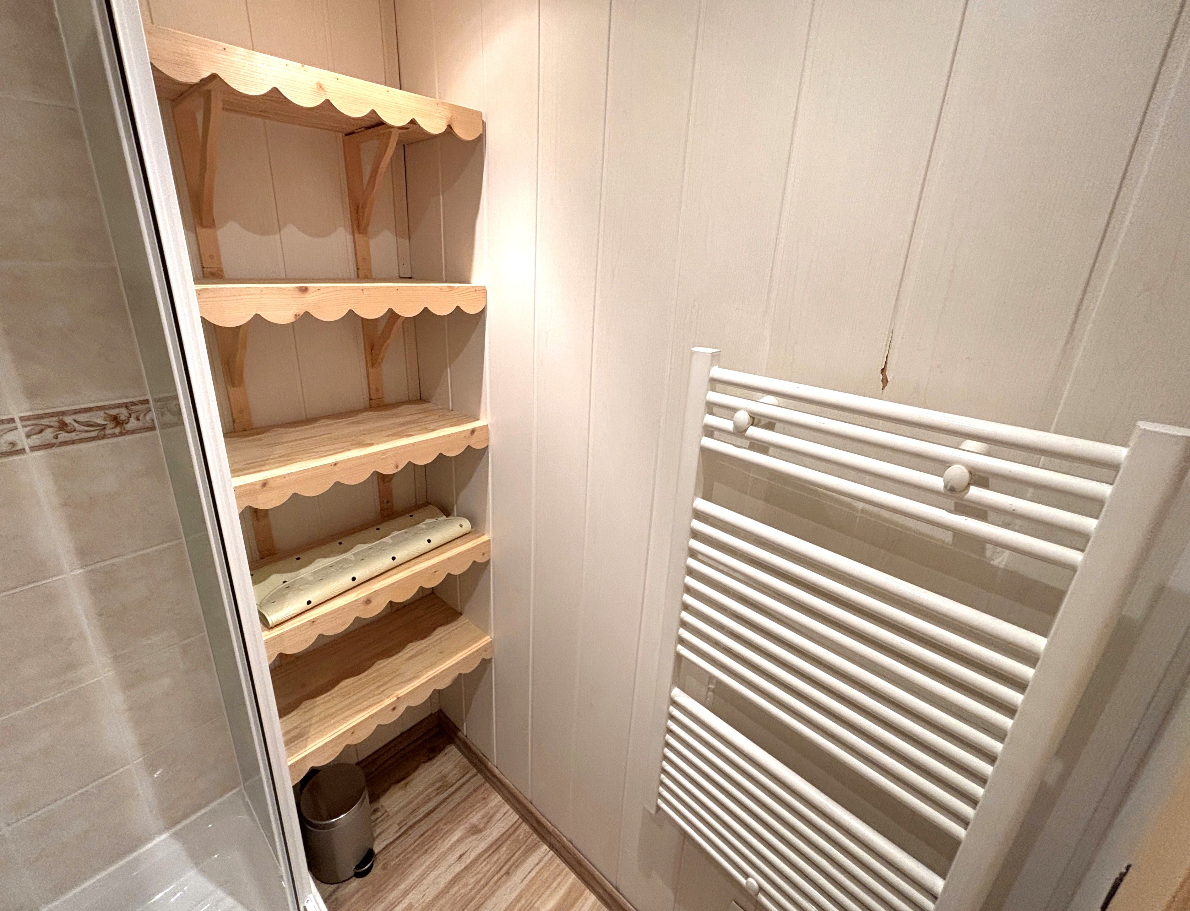 A narrow walk-in closet with wooden shelves and a white radiator.