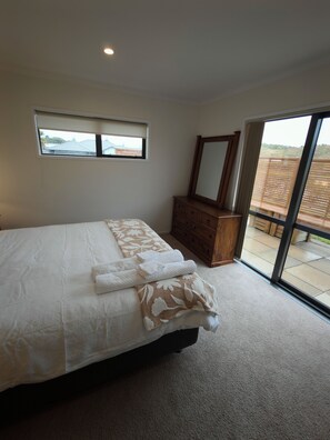 A bedroom with a bed, a dresser, a mirror, and a view through a glass door. - Beauty near the Ocean spacious four-bedroom home (New Plymouth)