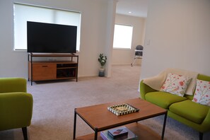 A living room with a flat-screen TV, a wooden coffee table, a green sofa, and a small potted plant. - Beauty near the Ocean spacious four-bedroom home (New Plymouth)