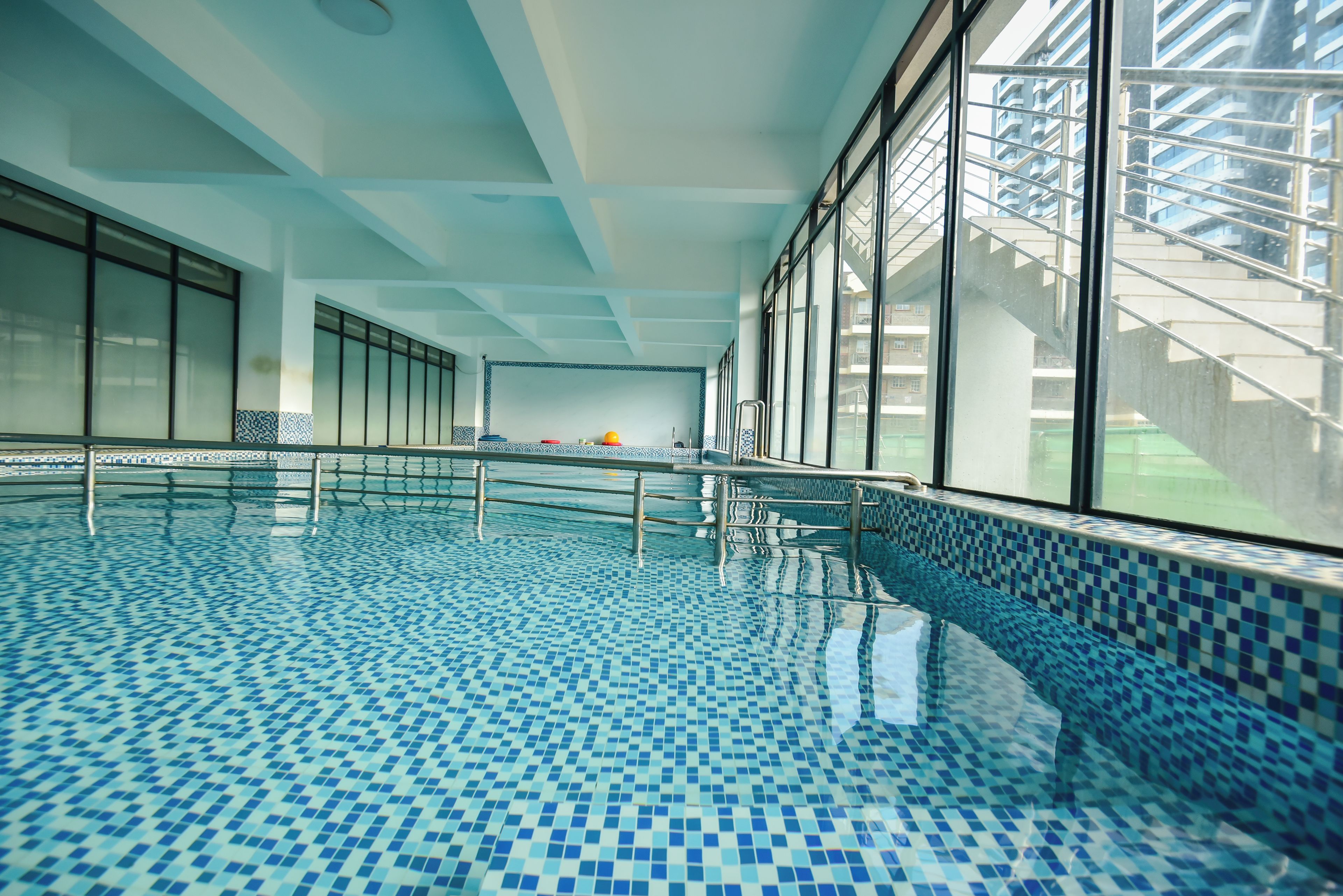 Une piscine intérieure à l’eau d’un bleu limpide, dotée d’un sol carrelé et de grandes fenêtres offrant une vue sur l’extérieur.