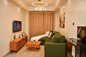 A modern living room with a sectional sofa, a wooden coffee table, a TV, and a painting on the wall. - 1-bedroom apartment in lovely Nairobi with fitness room access, Pool (Nairobi)