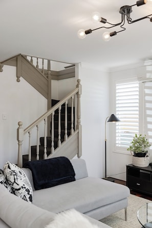 A modern living room with a staircase, a sofa, a floor lamp, and a window with blinds. - New York style meets laid-back Perth living at The Kensington New Yorker.  Enjoy light-filled interiors, beautiful character and a private outdoor space, perfectly positioned near Curtin University,  South Perth, Victoria Park and Perth CBD. (Kensington)