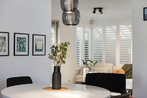 A dining area with a round table, a vase with flowers, and framed pictures on the wall. - New York style meets laid-back Perth living at The Kensington New Yorker.  Enjoy light-filled interiors, beautiful character and a private outdoor space, perfectly positioned near Curtin University,  South Perth, Victoria Park and Perth CBD. (Kensington)