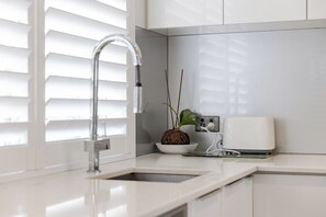 A modern kitchen with a stainless steel faucet, a bowl with a plant, and a coffee maker on the counter. - New York style meets laid-back Perth living at The Kensington New Yorker.  Enjoy light-filled interiors, beautiful character and a private outdoor space, perfectly positioned near Curtin University,  South Perth, Victoria Park and Perth CBD. (Kensington)