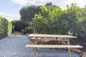 Une table de pique-nique en bois, posée sur du gravier, avec en arrière-plan un citronnier et un arbuste taillé avec soin.