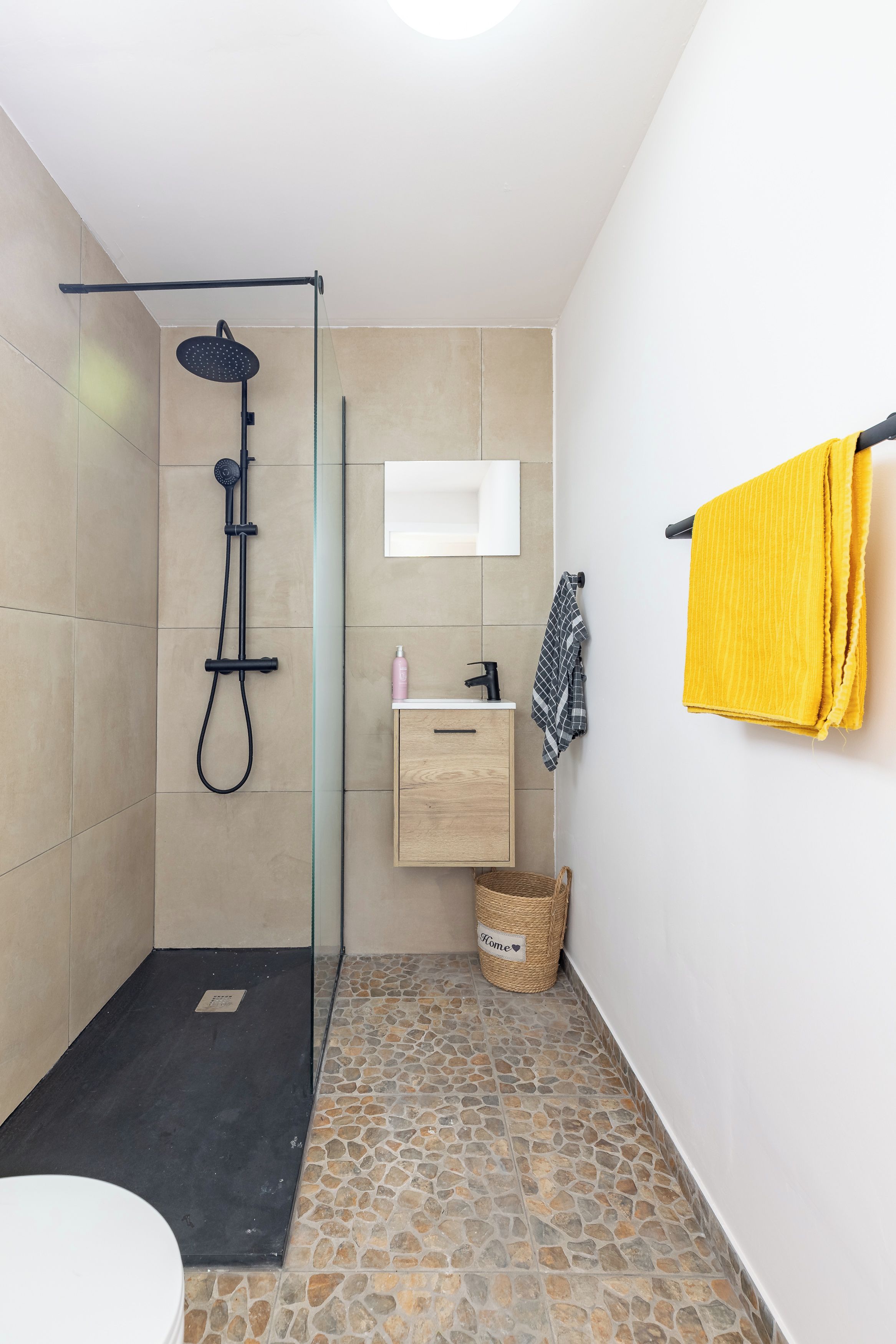 Un baño moderno con cabina de ducha de vidrio, un mueble de madera, un espejo y una toalla amarilla.
