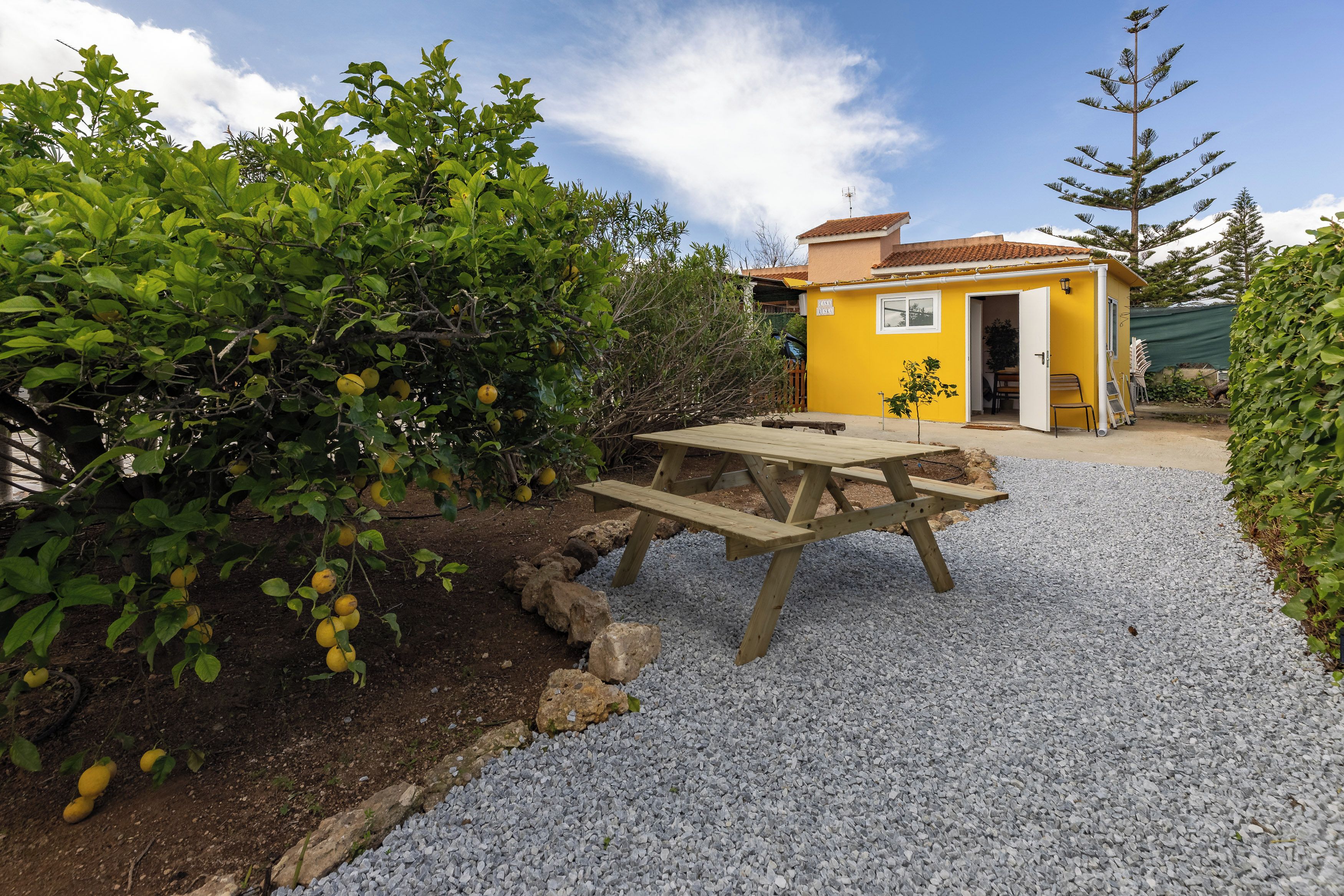 A yellow building with a patio table and a gravel path.
