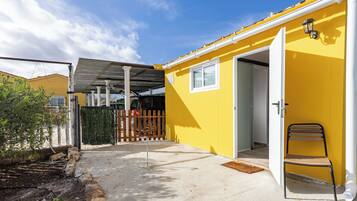 Un edificio amarillo con un patio cubierto, cerca de madera y una silla afuera.