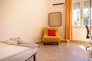 Una camera d'albergo con un letto, una sedia, uno specchio e una finestra con tende.