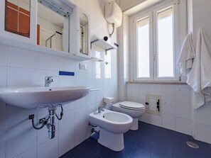 Un bagno con un lavandino, due servizi igienici, uno specchio e una finestra.